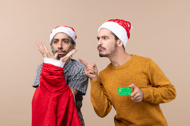 两个前视图两个家伙一个拿着圣诞老人的外套 另一个拿着信用卡看着米色背景上的东西男人前面风景