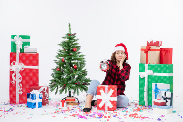 人前视图年轻女子坐在圣诞礼物周围拿着白色墙上的时钟快乐圣诞节礼物