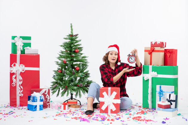 礼物前视图的年轻女子坐在圣诞礼物周围拿着白色墙上的时钟抱着雪前面