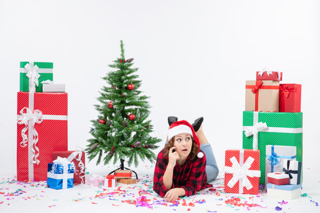 庆祝年轻女子躺在白色墙壁上的圣诞礼物和小圣诞树周围的正视图女人冬青节日