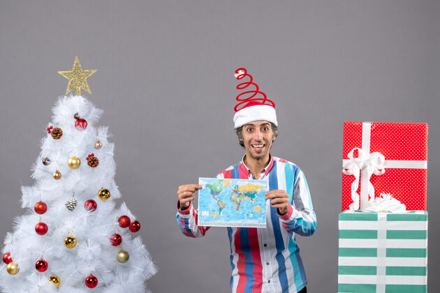 春天前视图笑脸男子与螺旋弹簧圣诞帽举行地图附近的白色圣诞树和复制空间礼品盒地图大笑的人