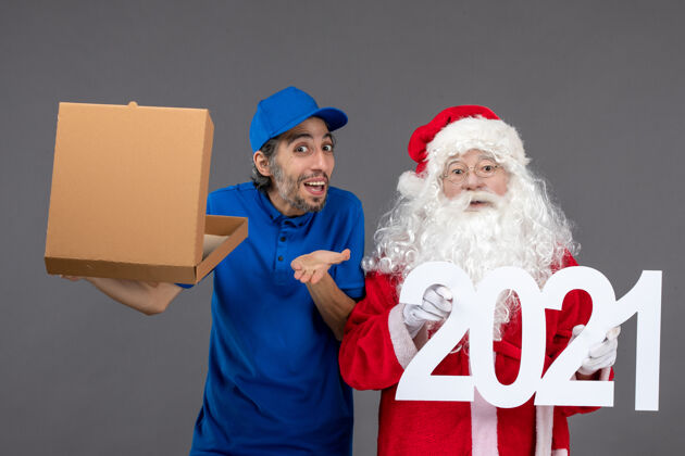 圣诞快乐圣诞老人的正面图 灰色的墙上有男信使拿着购物袋和食品盒圣诞人快乐