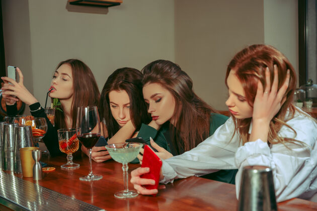 女朋友在酒吧喝饮料的女性朋友 她们坐在一张摆着鸡尾酒的木桌旁 穿着休闲服一起手酒