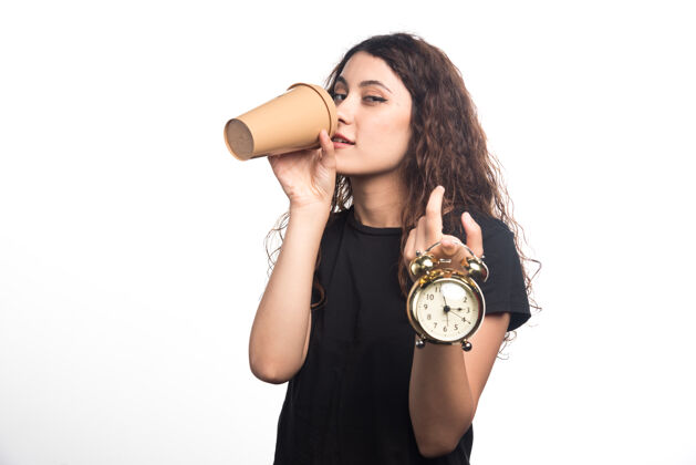手表手拿时钟的年轻女孩在白色背景上显示时间和喝咖啡…高质量的照片人年轻人女孩