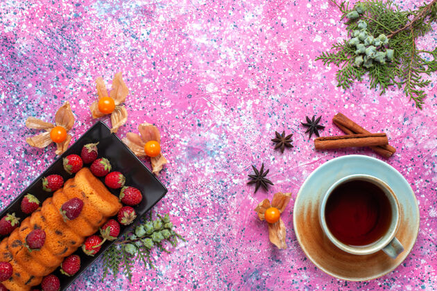 蛋糕在粉红色的桌子上 可以俯瞰美味的蛋糕 红色草莓和一杯茶美味红色甜