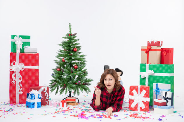 礼物正面图年轻女性躺在白色背景上的圣诞礼物和圣诞树周围圣诞新年情感礼物彩色雪女性圣诞树