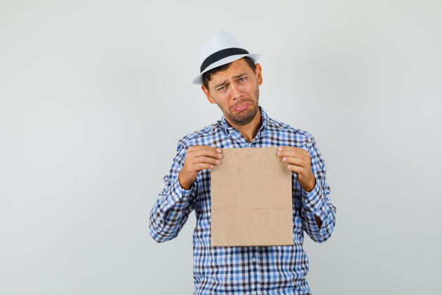 男人年轻人拿着纸袋 穿着格子衬衫 戴着帽子 神情沮丧工作室相机年轻