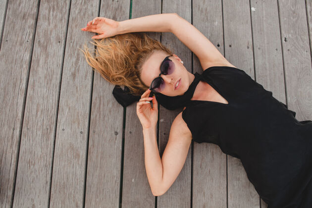 女孩奢华性感迷人的女人穿着黑色连衣裙躺在地上戴着墨镜 暑假 俯瞰模特休闲服饰