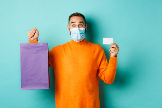 医疗面具Covid-19 流行和生活方式的概念快乐的男性客户显示信用卡和紫色时髦酷购物