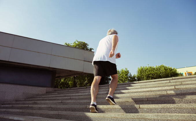 慢跑在城市街道上戴着臂章或健身的高级男子跑步者高加索男模在夏天的早晨练习慢跑和有氧训练健康的生活方式 运动 活动理念运动员运动草地