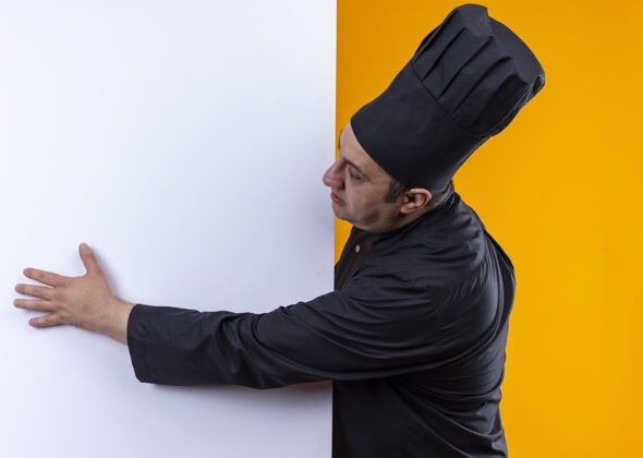 持有站在剖面图中年男性厨师在厨师制服举行黄色背景白色墙壁与复制空间中年制服厨师