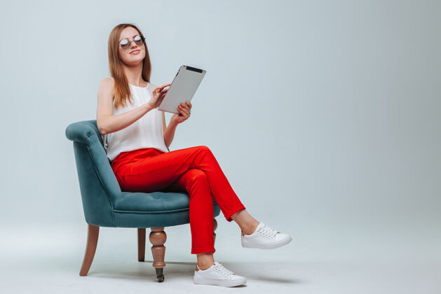秘书穿着红裤子的女孩坐在椅子上用她的平板电脑教育平板电脑快乐