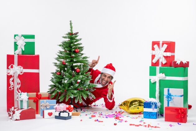 圣诞老人圣诞气氛与年轻有趣的圣诞老人躲在圣诞树附近的礼物在白色背景上不同的颜色不同冬青年轻