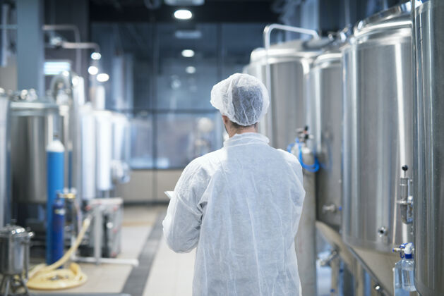 自动化穿着白色防护服的工艺师走过食品厂生产线检查质量控制机器制药