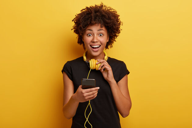 阅读快乐热情的女性手持连接立体声耳机的智能手机设备 积极微笑手机在线发送