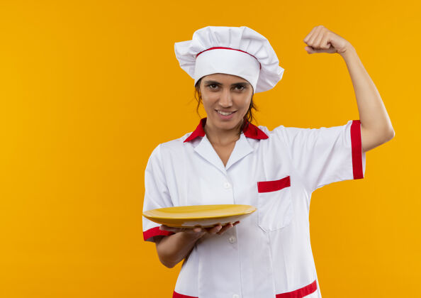 展示面带微笑的年轻女厨师穿着厨师制服拿着盘子 用复制空间表现出强烈的姿态穿着制服厨师