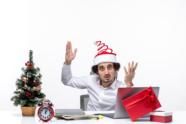 电脑新年气氛与困惑的年轻商人与有趣的圣诞老人帽子问一些东西在白色背景的办公室圣诞老人问年轻人