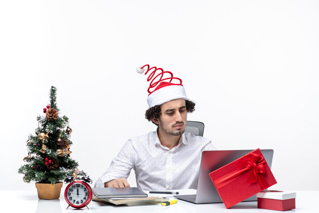 人专注的年轻商人戴着有趣的圣诞老人帽子在白色背景的办公室庆祝圣诞节电脑圣诞节年轻商人