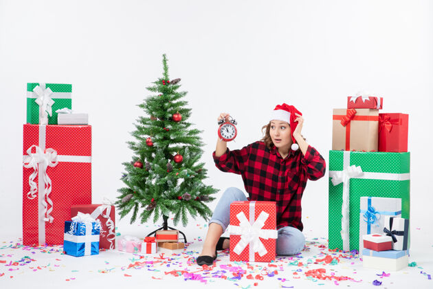 十二月前视图的年轻女子坐在圣诞礼物周围拿着白色墙上的时钟礼物节日人