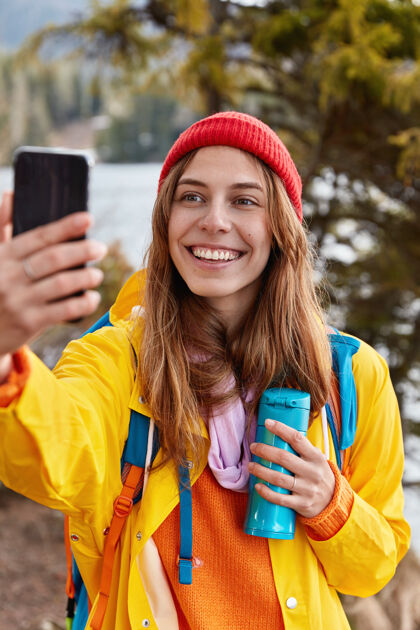 远足快乐的年轻旅行者开心地微笑 用手机自拍 穿着黄色的休闲服 拿着热水瓶喝茶 在美丽的森林里休闲乐观照片咖啡
