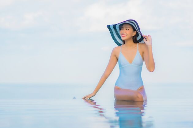 度假村肖像美丽的亚洲年轻女子放松微笑周围的室外游泳池在酒店度假村休闲比基尼水疗
