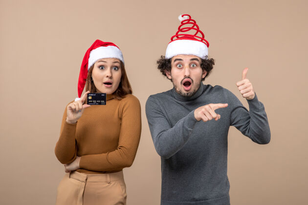 圣诞老人圣诞节心情激动满意酷情侣戴红色圣诞老人帽女人出示银行卡男人指着什么兴奋家庭酷情侣