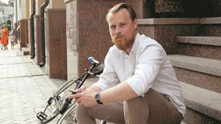 自行车城市街道上坐在石阶上的笑容可掬的留着胡子的时髦男人的色调肖像旅游交通肖像