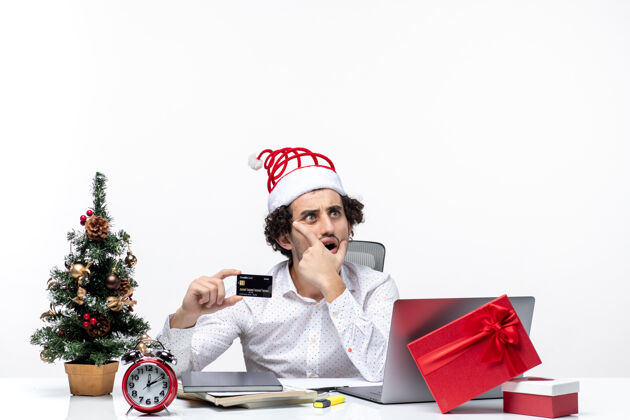 商务人士一个戴着圣诞老人帽子 拿着银行卡的商人惊讶地看着办公室里白色背景的东西人惊讶看