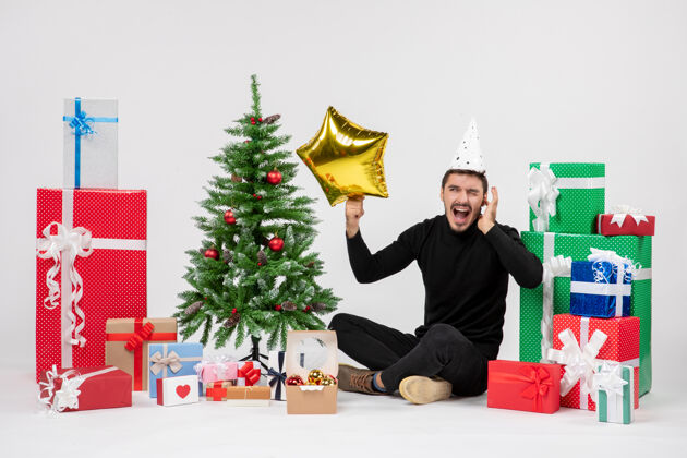 庆祝年轻人围坐在礼物旁边 拿着金星在白墙上圣诞快乐办公室抱着