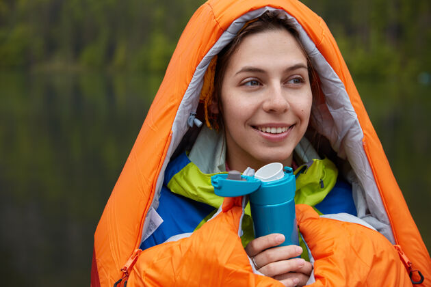 个人乐观的欧洲年轻女子头像喝热饮料 拿着烧瓶 裹在橙色睡袋里女性饮料人类
