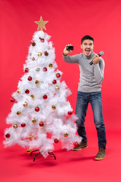 圣诞树圣诞气氛与骄傲的家伙站在装饰圣诞树附近 手持麦克风和电话站立装饰举行