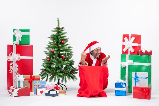 圣诞树有趣的年轻人打扮成圣诞老人与礼物和装饰圣诞树上的白色背景圣诞老人年轻人礼物