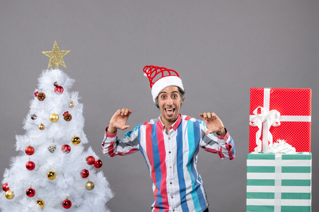 打开正面图：快乐的年轻人张开双手站在白色圣诞树旁开朗人微笑