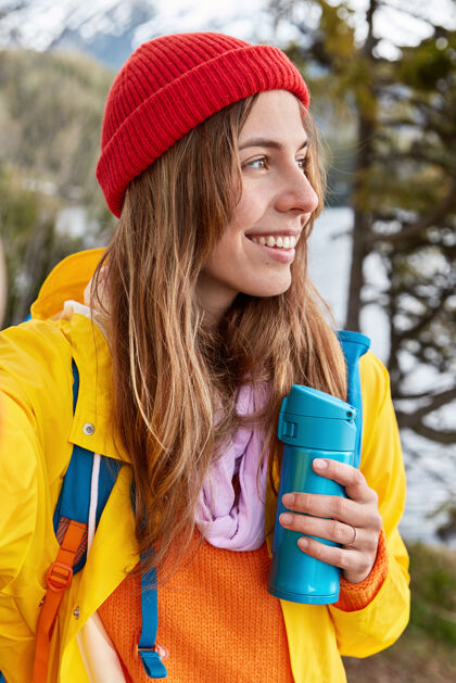 背包客微笑的女游客戴着红帽子 黄外套 伸出手 用不可辨认的装置自拍背包采取自然