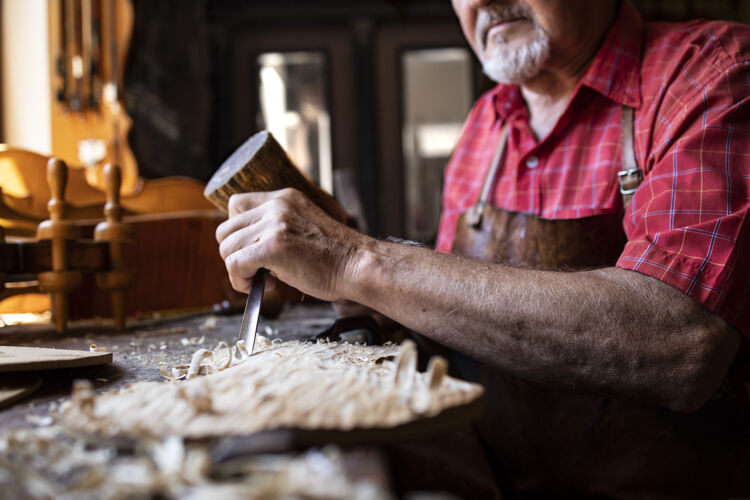 手工一个老派的资深木匠 拿着刀和锤子在他的木工车间里雕刻木板传统硬木工匠