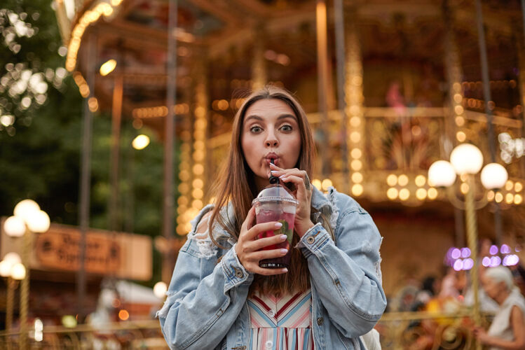 女人可爱的长发黑发女人 穿着休闲服 一边喝着稻草柠檬水 一边走在公园里的景点里 看着缩紧的额头情绪年轻牛仔裤