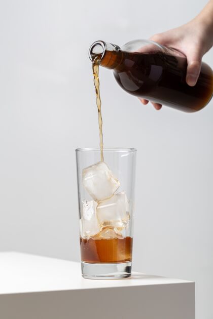冰块垂直特写一个人倒在一个杯子里的冰块在桌子上的茶饮料水灯