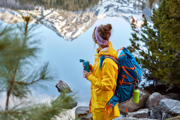 冒险徒步旅行的女人在山上的湖边停下来 背着背包 拿着热饮料的保温瓶 探索新事物独自背包放松