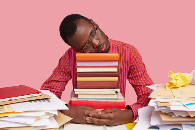倾斜心烦意乱疲惫的黑人在一堆书上小睡 通宵学习后睡觉 准备考试不快乐坐着考试