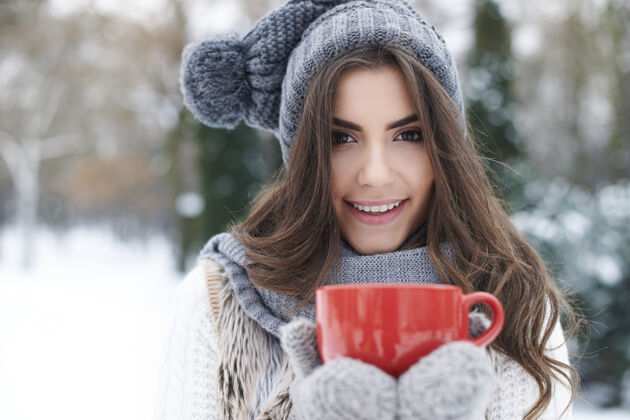 幸福美丽的年轻女子在冬天热身自然喝热巧克力
