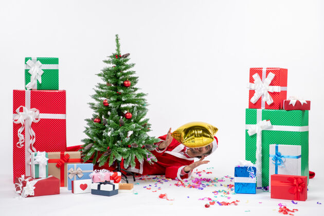 说谎圣诞心情与圣诞老人躺在圣诞树后附近的礼物在不同颜色的白色背景股票照片冬青圣诞树圣诞老人