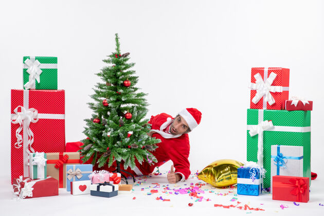 圣诞老人圣诞心情与年轻的圣诞老人躲在圣诞树附近的礼物在不同颜色的白色背景股票照片礼物股票圣诞