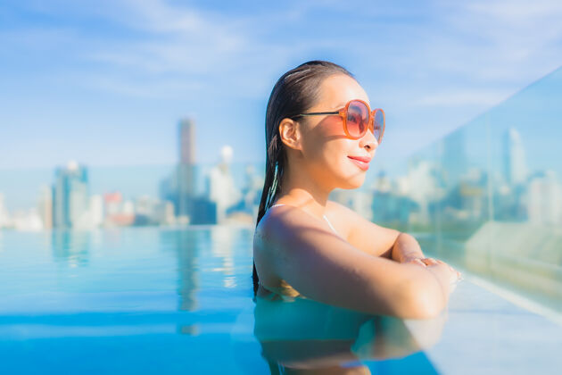 屋顶肖像美丽的亚洲年轻女子微笑放松休闲围绕室外游泳池与城市景观身体现代天际线
