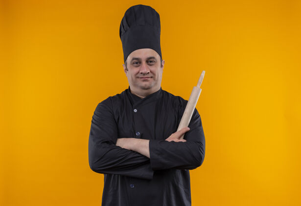 厨师身穿厨师制服的中年男厨师手拿擀面杖交叉放在黄色墙壁上 留有复制空间交叉厨师手