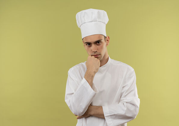 穿自信的年轻男厨师穿着厨师制服 将手放在下巴下 放在隔离的绿色墙壁上 留有复制空间制服下巴看起来