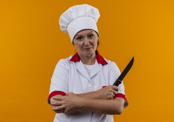 厨师身着厨师制服的中年女厨师双手交叉持刀站在隔离的黄色墙壁上 留有临摹空间拿厨师交叉