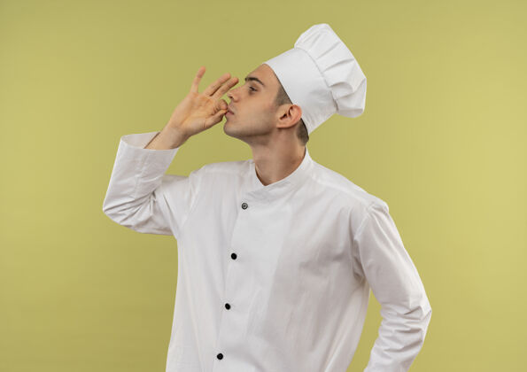 展示站在剖面图年轻的男厨师穿着厨师制服显示出美味的姿态与复制空间制服厨师手势