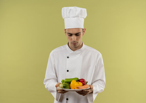 厨师想着年轻的男厨师穿着厨师制服看着盘子里的蔬菜用手抄空格蔬菜思考盘子