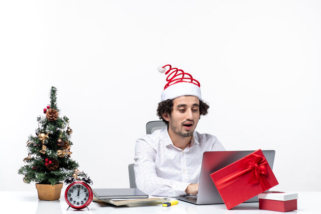 办公室快乐积极的年轻商人 戴着有趣的圣诞老人帽 在白色背景的办公室里看着笔记本电脑上的东西东西圣诞老人卖家
