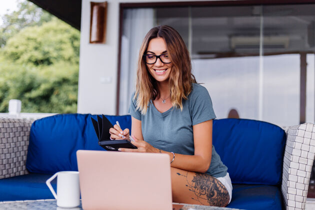 在线快乐的白种女人在家里用笔记本电脑做远程工作舒服的地方喝茶房子室内技术